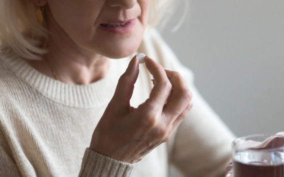 Mature senior middle aged woman holding pill and glass of water taking painkiller to relieve pain